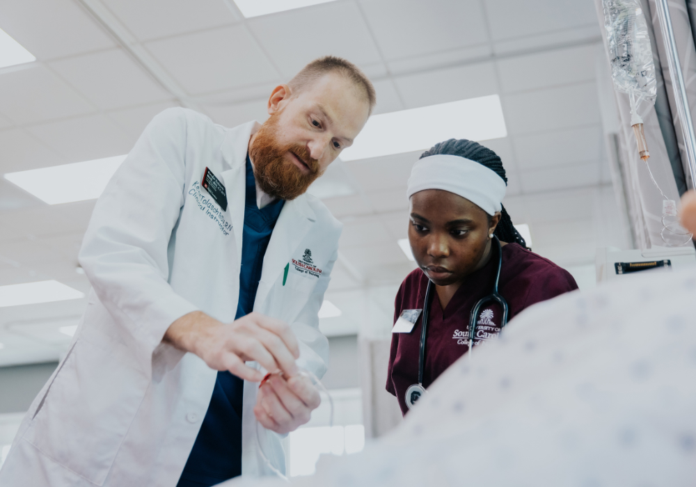 teacher in lab coat helping nursing student in scrubs place an iv on a mannequin
