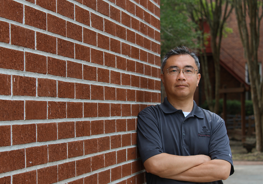 Math professor Wei-Kai Lai stands next to a brick wall on the USC Salkehatchie campus
