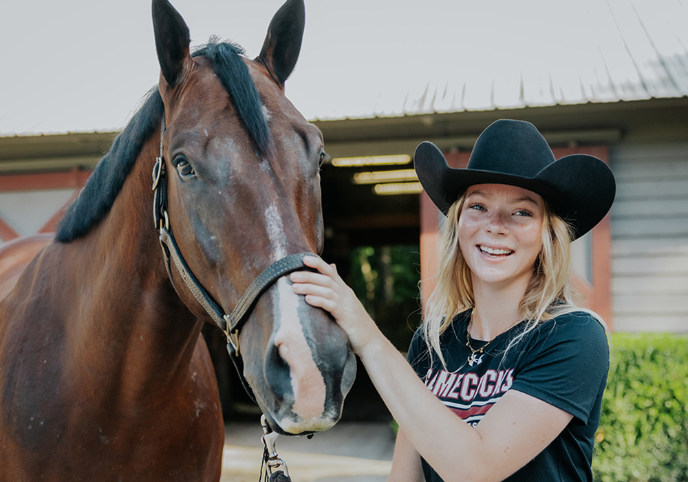 Ruby Voortmeyer stands smiling beside her horse.