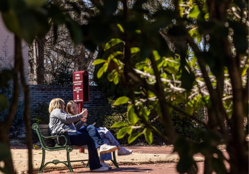 Two students on a bench on the USC campus taking a picture with their cellphone.