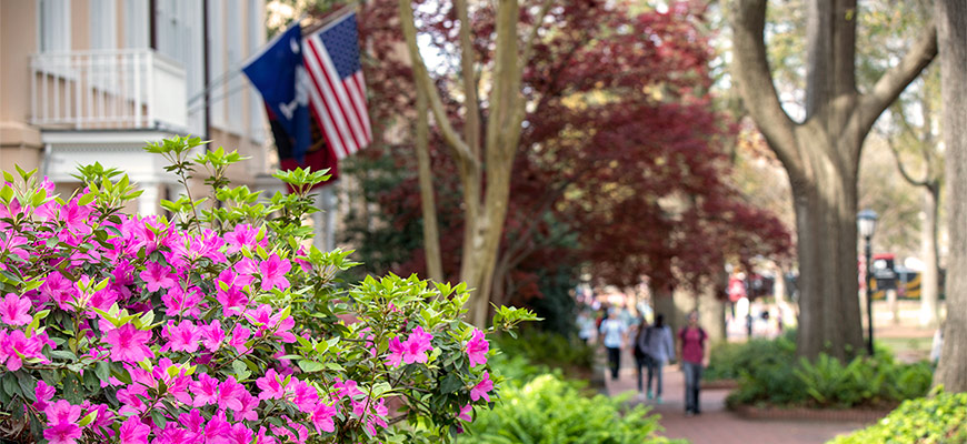 A South Carolina flag and an American flag hang behind a brightly blooming flower bush outside the president's residence