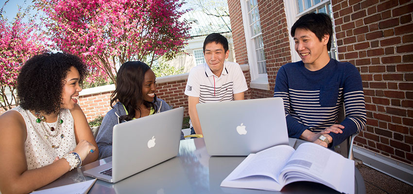 Four students sit at a table on the SJMC patio with laptops