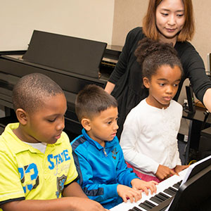 Children learning to play piano from instructor