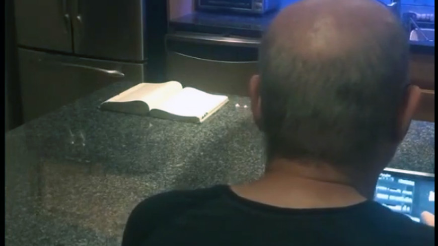 a man sits at a laptop with a book on the other side of the counter
