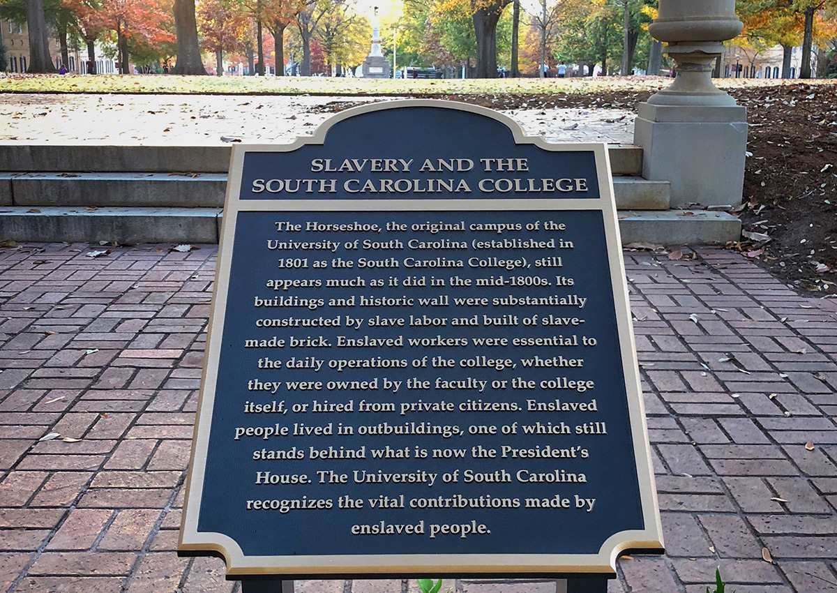 Plaque at the top of the horseshoe acknowledging the contribution of enslaved people building the original University of South Carolina campus. It says "Slavery and the South Carolina College. The horseshoe, the original campus of the University of South Carolina (established in 1801 as the South Carolina College), still appears much as it did in the mid-1800s Its buildings and historic wall were substantially constructed by slave labor and built of slave-made brick. Enslaved workers were essential to the daily operations of the college, whether they were owned by the faculty or the college itself, or hired from private citizens. Enslaved people lived in outbuildings, one of which still stands behind what is now the President's House. The University of South Carolina recognizes the vital contributions made by enslaved people." 