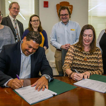 Megan Brown sits at a table with a man as they sign documents while others look on