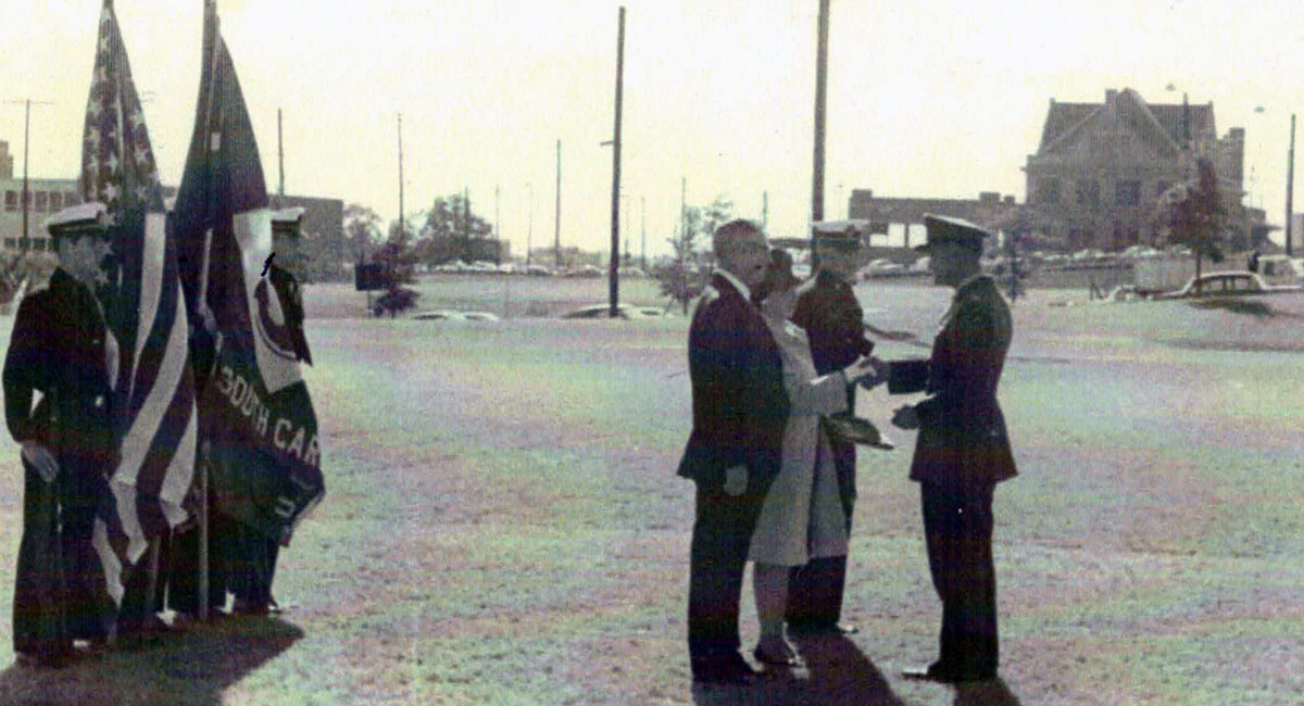 Archival photo with a color guard on the left and civilians on the right receiving medals for UofSC graduate Joseph Hart who was killed in the Vietnam War. 