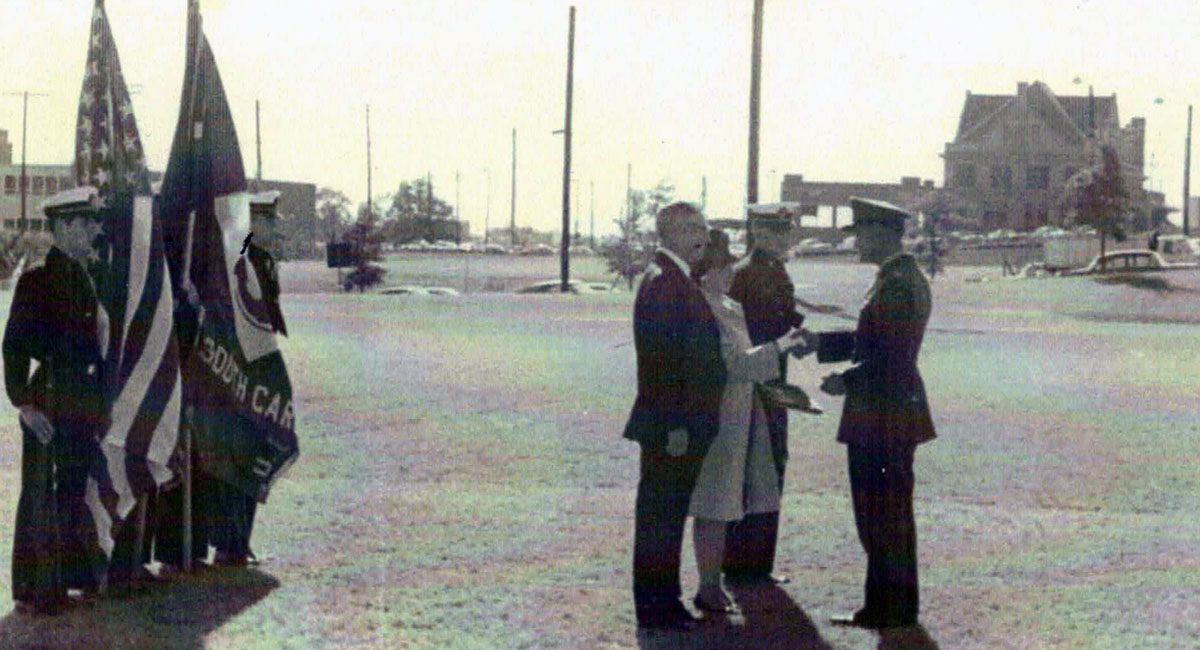 Archival photo with a color guard on the left and civilians on the right receiving medals for UofSC graduate Joseph Hart who was killed in the Vietnam War.