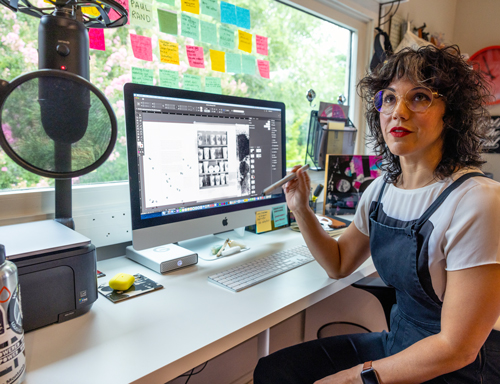 meena khalili sits at her computer in front of a window with a variety of sticky notes on the window