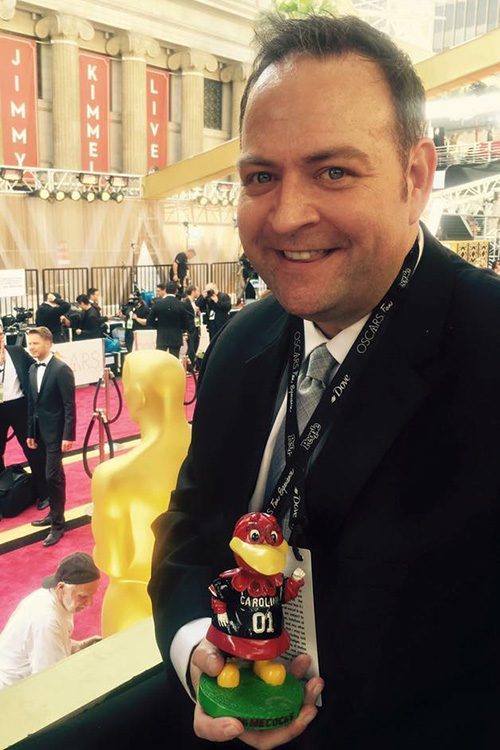 Alumnus Stephen Brown holds a Cocky figurine with a red carpet in the background