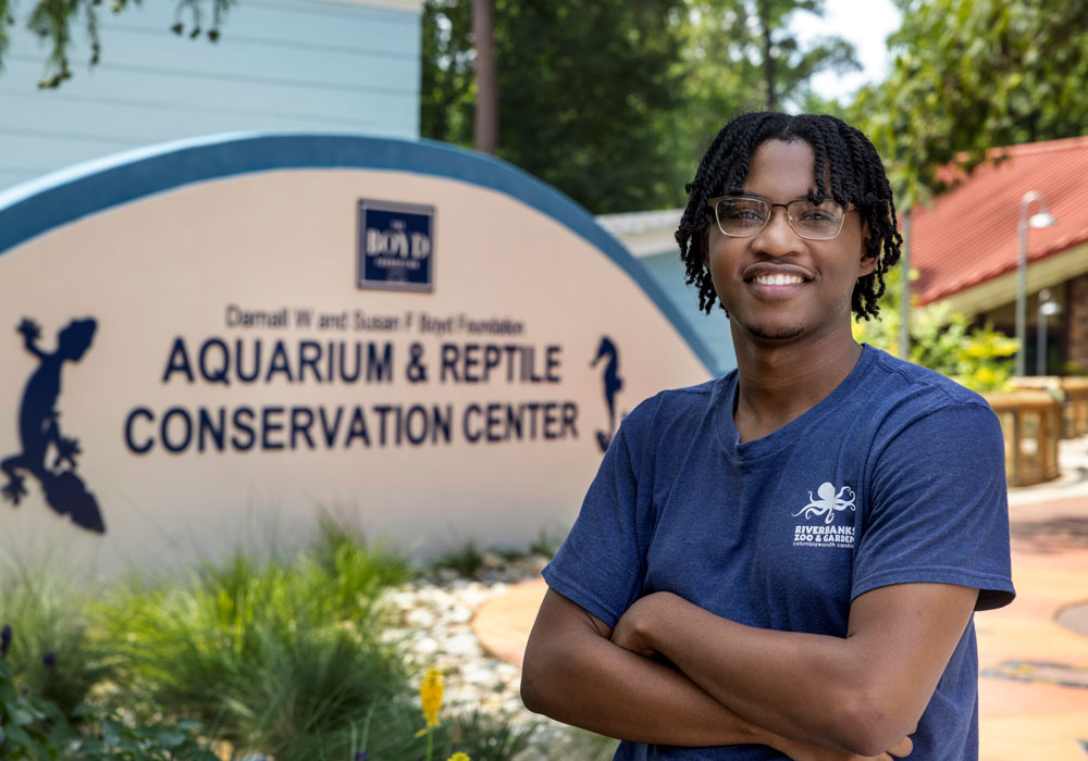 Trenton King stands in front of a sign that says "aquarium and reptile conservation center"