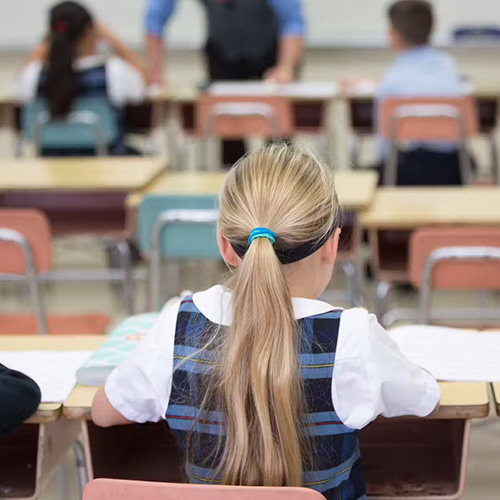 A Catholic schoolgirl is seen from behind in classroom.