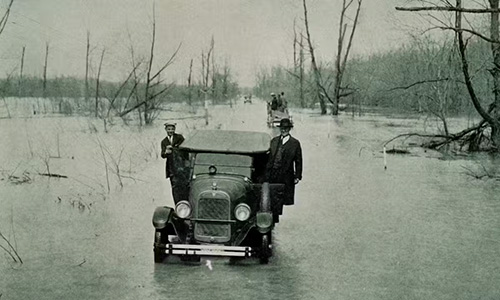 Two men stand outside their truck, which is stuck in rising waters