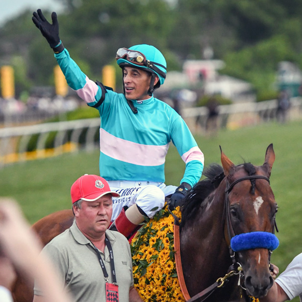 jockey on horseback waves as his horse is walked to the winner's circle