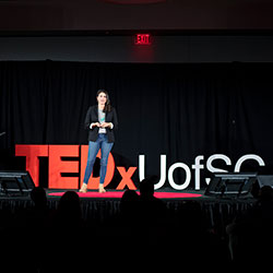 Kassy Alia at the 2018 event standing in front of red TEDx sign.