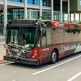 The new cobranded COMET/UofSC Transit bus in front of the Darla Moore School of Business
