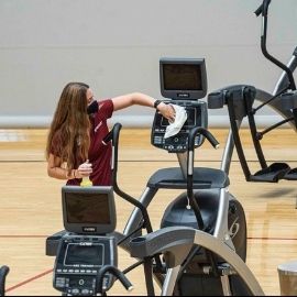 A student employee at one of the campus gyms sanitizing exercise equipment