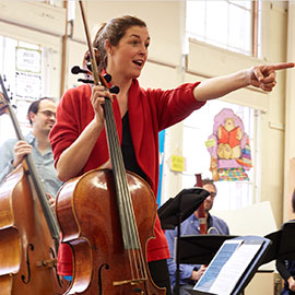 School of Music assistant professor Claire Bryant holds a cello while pointing at a fellow musician.