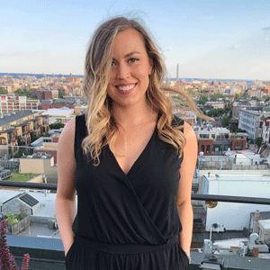 UofSC alumna Hali Kerr stands on a rooftop with a city skyline behind her