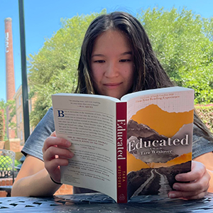 A student reads Educated, showing Brooke Daniels' cover design.