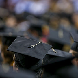 Students in mortarboard caps sit in the Colonial Life Arena