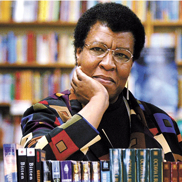 Author Octavia E. Butler in a multicolor jacket with poses with chin on hand in a Seattle bookstore.
