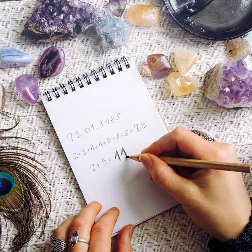 Hands writing numbers on a spiral notepad surround by crystals