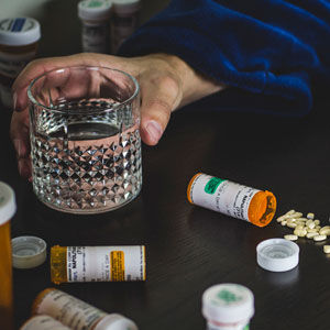 Man holding glass of water with prescription pills next to him on a table