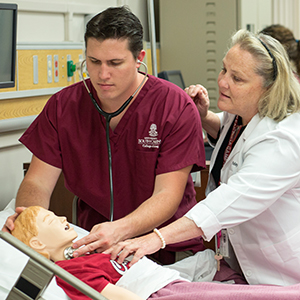 A nursing student practices on a mannekin while a professor observes. 