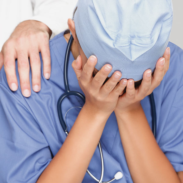 A healthcare worker wearing scrubs with his/her hands over face indicating frustration.