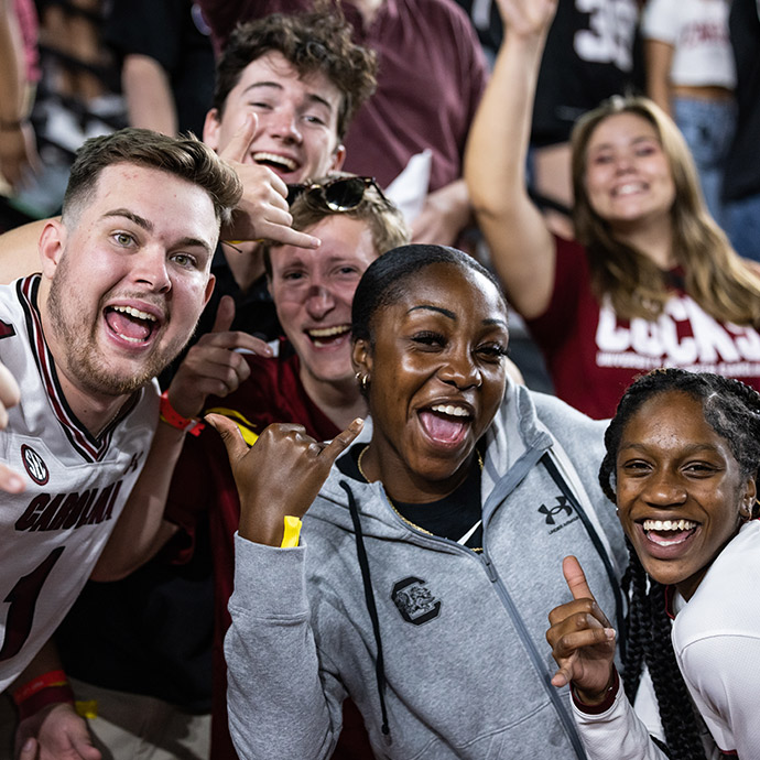 A group of students smiling at a USC football game using a spurs up hand sign.
