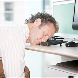 Man sitting in a desk chair resting his head on a keyboard 