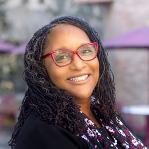  Dr. Gayenell Magwood wears a floral garnet and black scarf and red glasses frames.