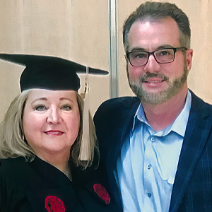 Sandra Edwards, posing with her husband, in a cap and gown, celebrates graduating with a master's degree from the Darla Moore School of Business.