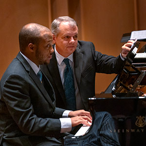 Two men sit at a piano