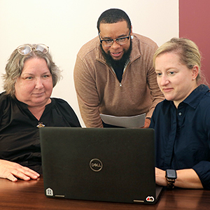 Landon Pitts looks at a laptop alongside two peers.