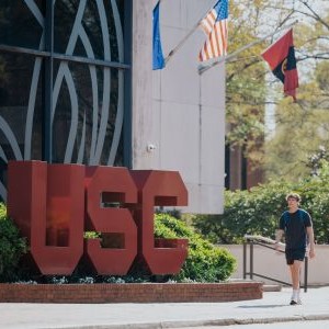 Student walking in front of a USC sign at the Russell House student union.