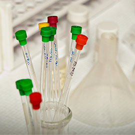 thin test tubes with colorful tops stand in a large beaker