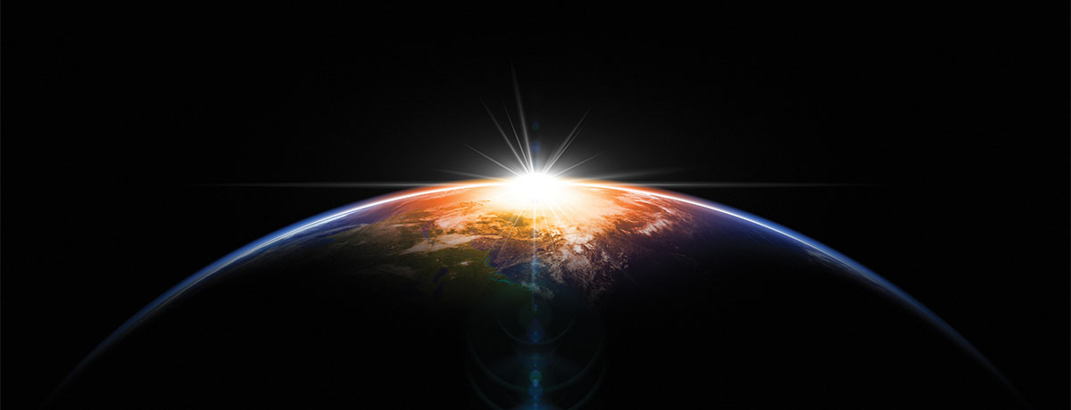 The sun cresting over the earth from outer space. 