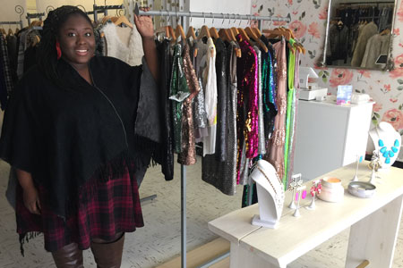 Hawa Lukulay, alumna and owner of Messie's Closet, poses next to a clothesrack.