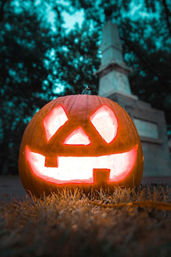 A warmly lit jack o'lantern photographed sitting in the grass of UofSC's historic horseshoe