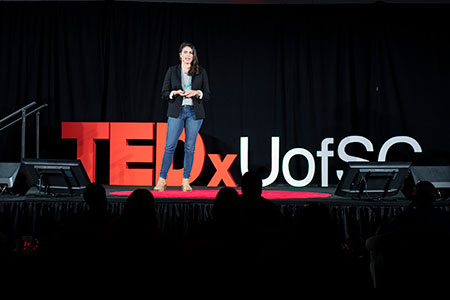 Kassy Alia standing on a stage with red TEDx logo in the background.