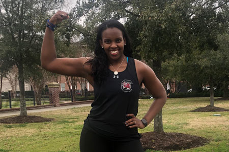 Group X fitness instructor, Elizabeth Thompson standing outside flexing her bicep