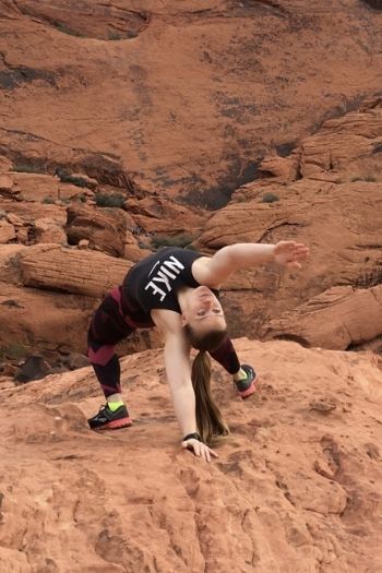 3rd year physical therapy doctoral candidate, jordan bartholf, cortorting her body into a one handed back bend on what appears to be large red rocks