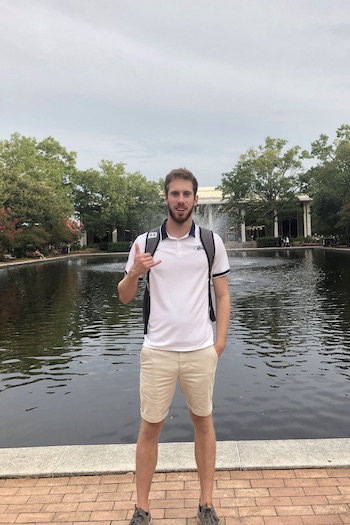 Sam Hopler, student employee for Gamecock Entertainment, posing with "spurs up" and his backpack on in front of the fountainn in front of the Thomas Cooper Library.