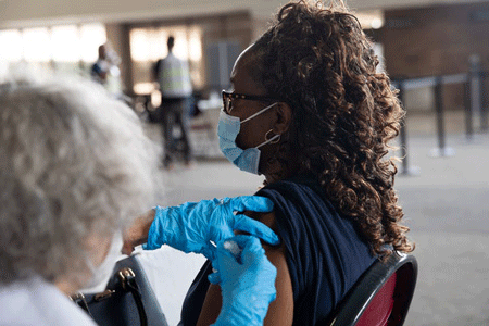 A woman receives a vaccination from a health care worker wearing blue latex gloves