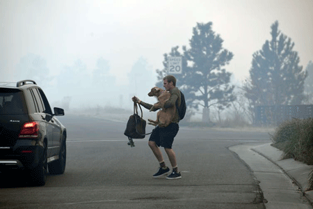 A man carried a dog and backpack to a waiting car in a smoky neighborhood as they prepare to evacuate from a wildfire.