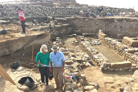 Researchers stand near the ruins of ancient walls, with the destruction layer about midway down each exposed wall