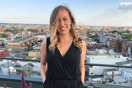 UofSC alumna Hali Kerr stands on rooftop with a city skyline behind her