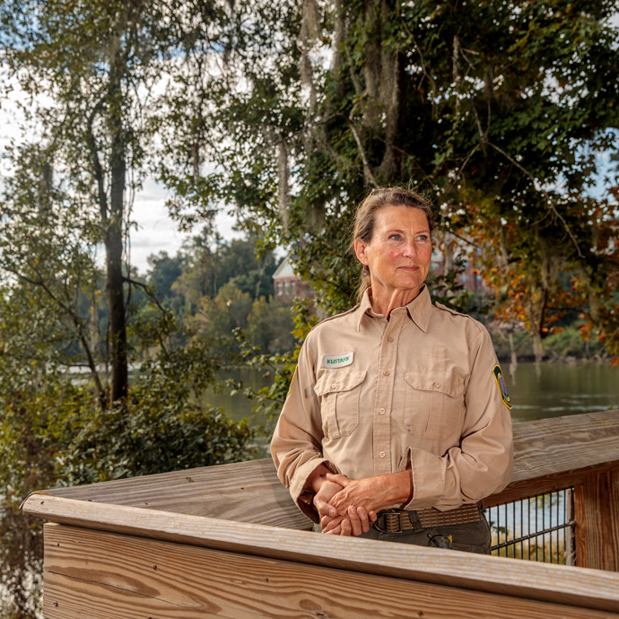 Portrait of Karen Kustafik leaning on a wooden railing.